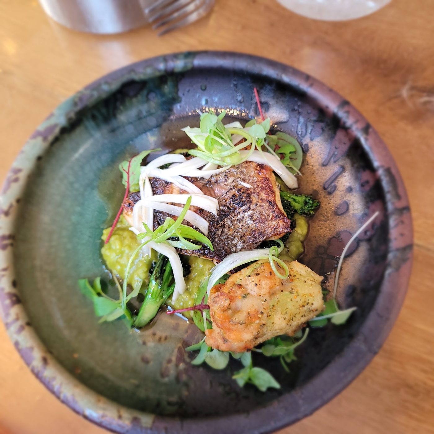 A fish dish with herbs and pickled onion in a dark bowl